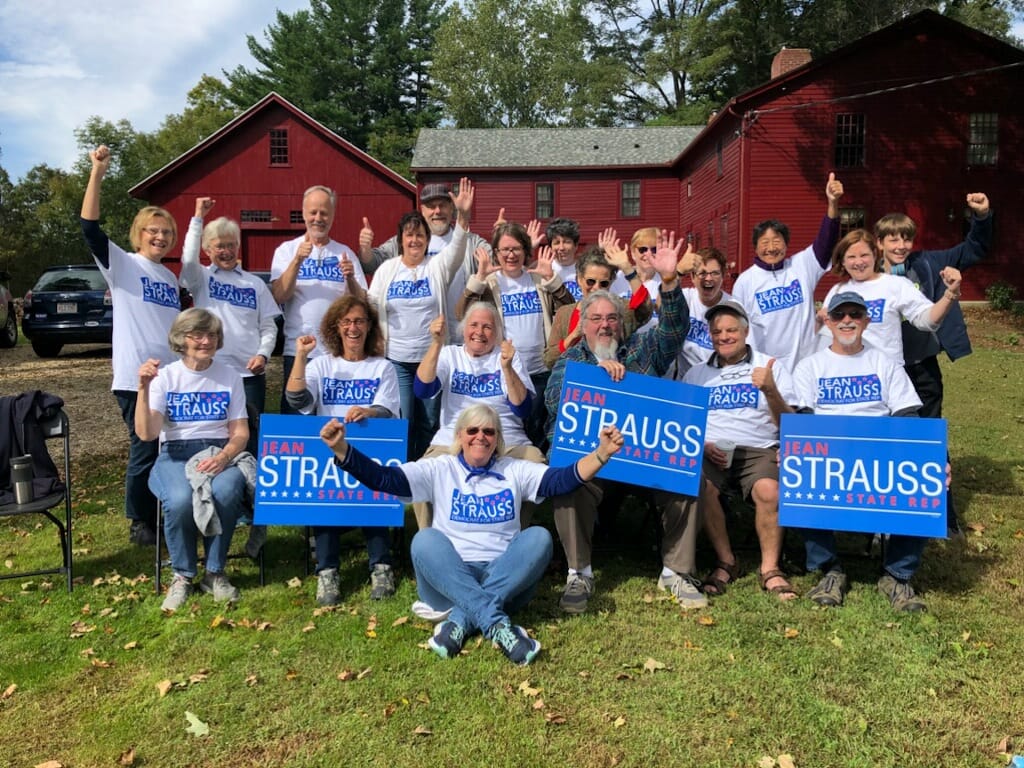 A group of people wearing shirts and displaying signs for Jean Stauss for State Representative.